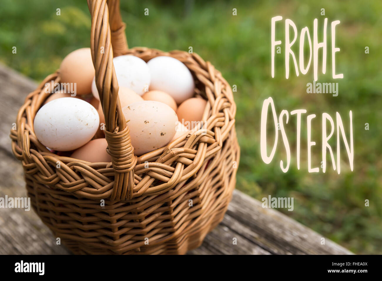 basket with white and brown bio eggs, green meadow in the background, german words frohe ostern which means happy easter Stock Photo