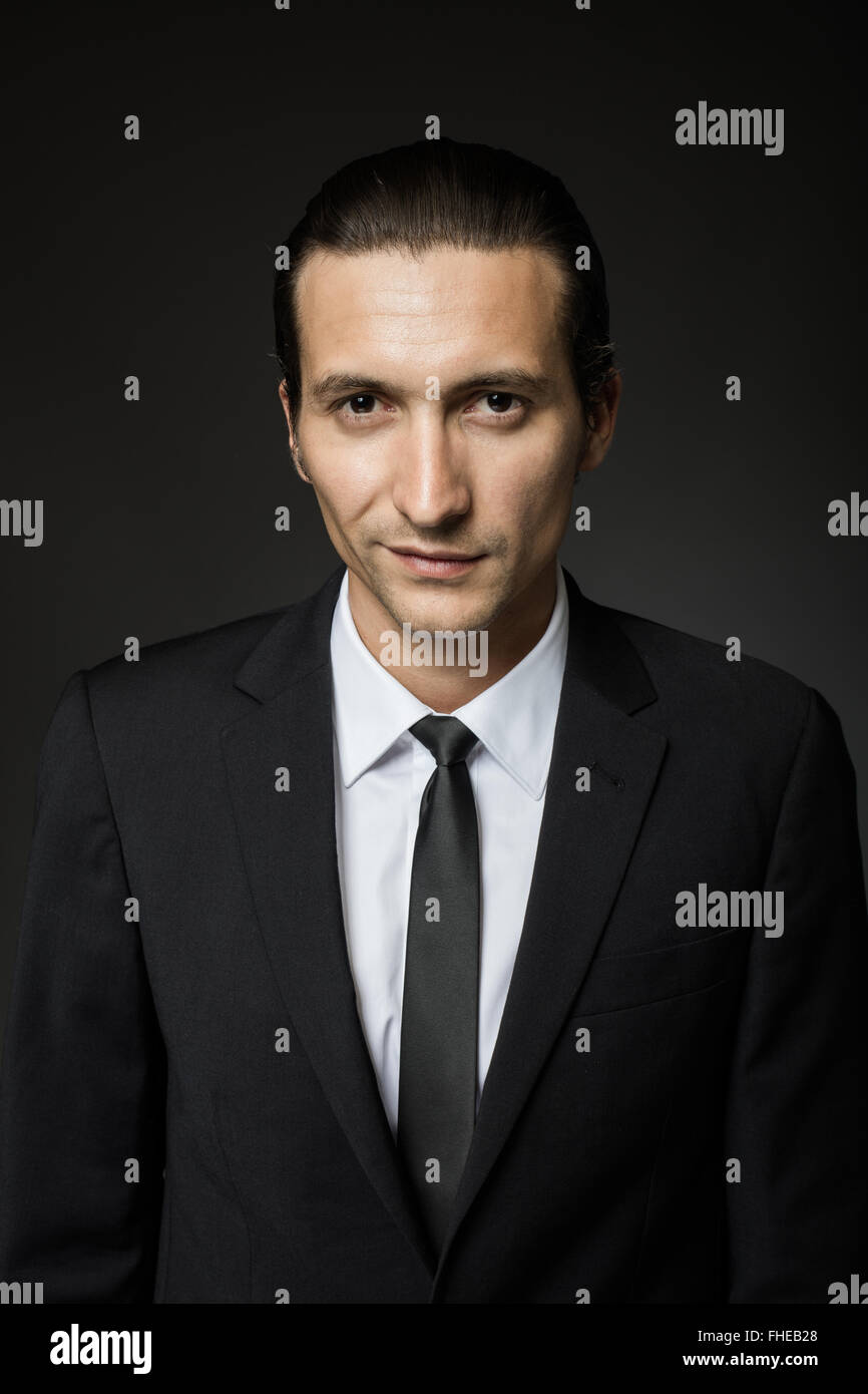 portrait of an attractive mysterious man in black suit and tie on dark ...