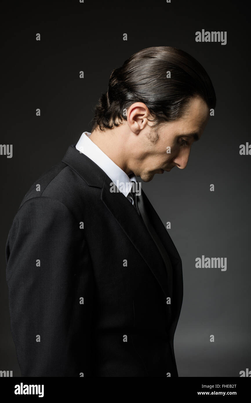 portrait of an attractive mysterious man in black suit and tie on dark ...