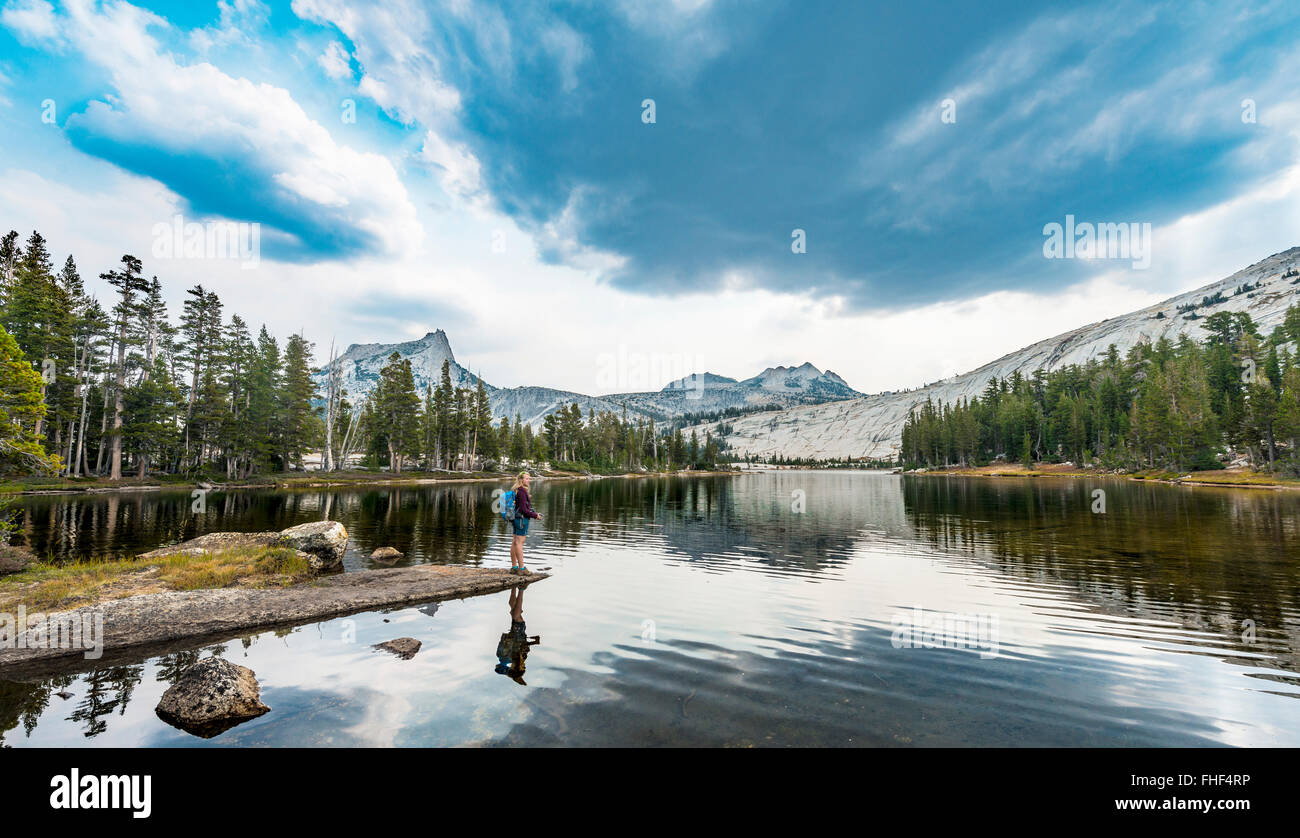 Hiker is standing on a lake, Lower Cathedral Lake, Sierra Nevada, Yosemite National Park, California Stock Photo