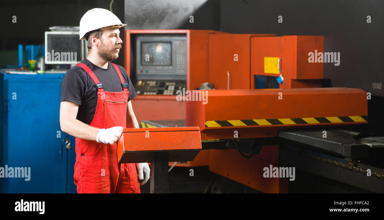 front view of a worker looking in the distance, wearing red overalls, white protective helmet and gloves, standing next to the c Stock Photo