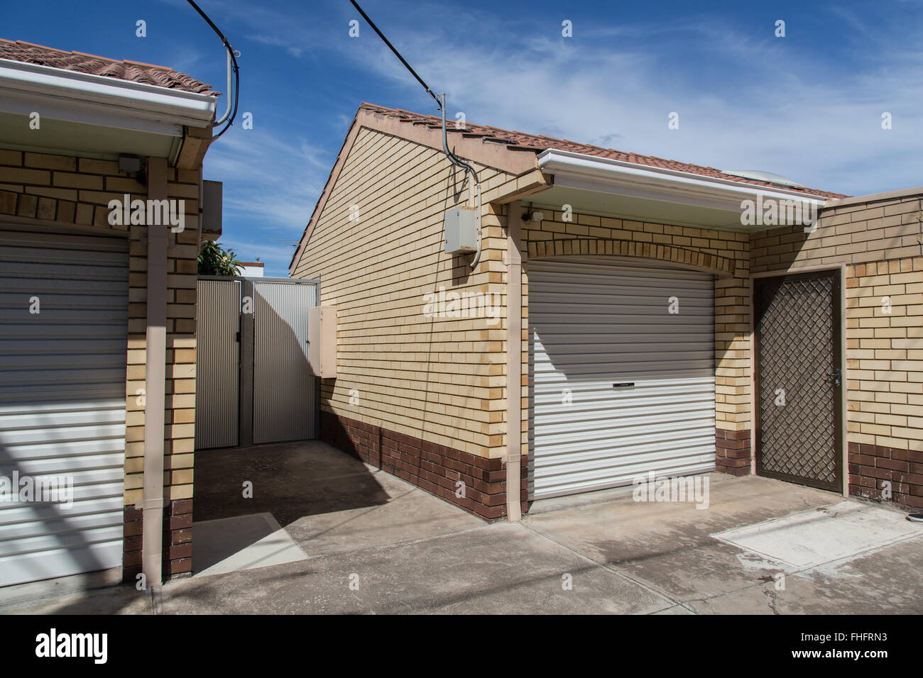 very simple house yard and garage, all shutters and door closed, single greenery behind metal gate, brick cladding Stock Photo