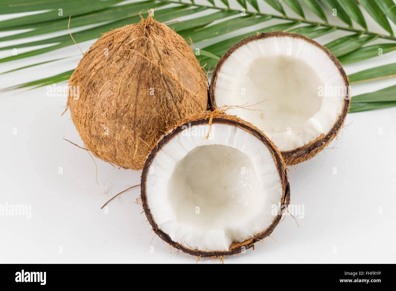 Halved and whole fresh coconuts with coconut leaves on white Stock Photo