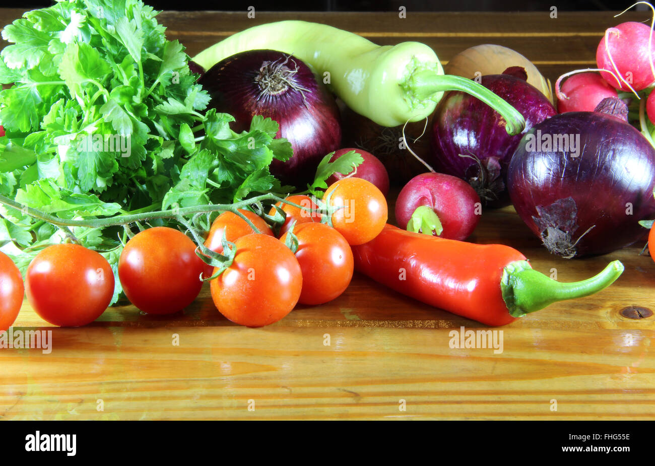 Peppers, tomato, radish, parsley and onions scattered on an old wooden table Stock Photo