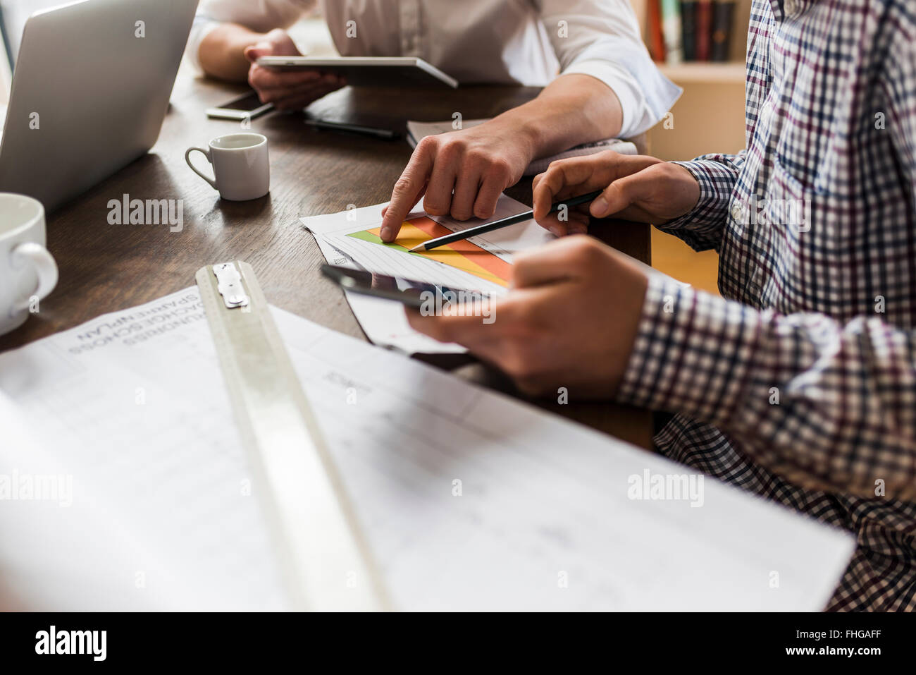 Colleagues at desk with smartphone, diagram and construction plan Stock Photo
