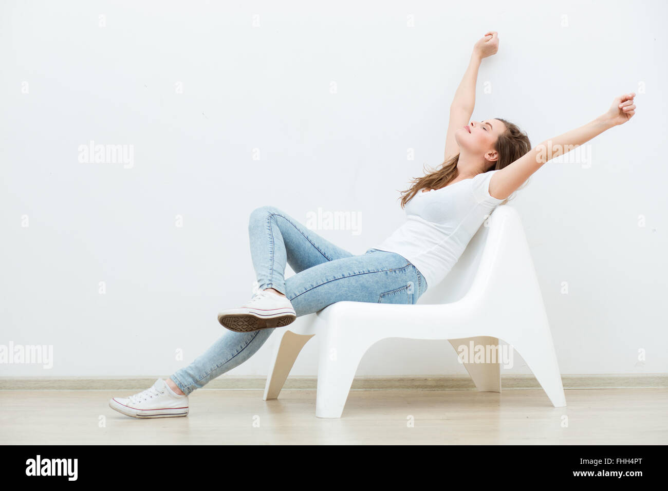 single happy young woman sitting on a white chair in an empty room, thinking on something Stock Photo
