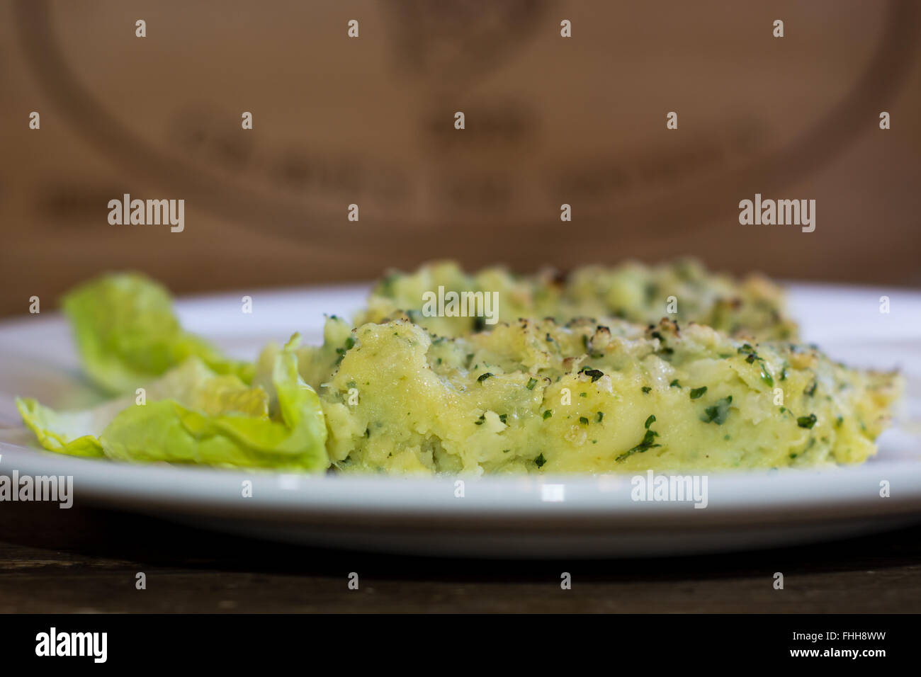 Fish pie on plate from side. Fish pie with potato and herbs served with olive oil and lettuce Stock Photo