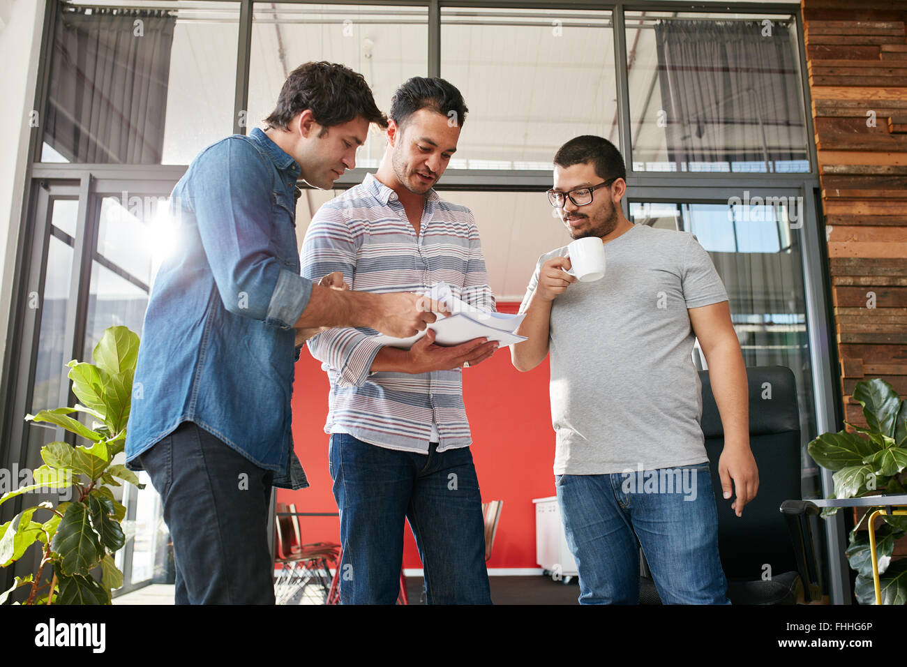 Group of businesspeople discussing paperwork in office. Three young men meeting in office. Stock Photo