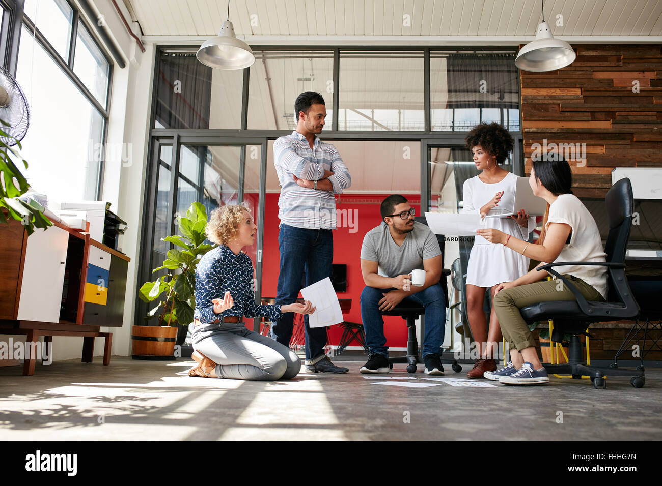 Creative team having a discussion on new design project in office. Project plan laid on floor with coworkers meeting and discuss Stock Photo