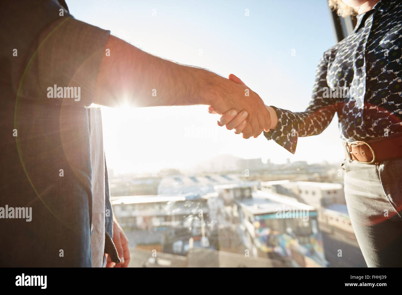 Handshake of two associates with sunlight. Male executive shaking his hand with female colleague, focus on hands. Stock Photo