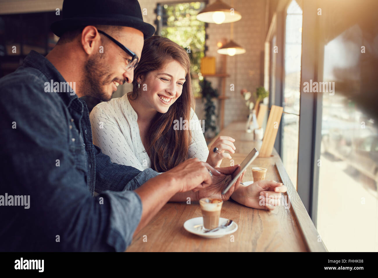 Happy couple in a coffee shop surfing internet on digital tablet. Young man and woman in a restaurant looking at touch screen co Stock Photo