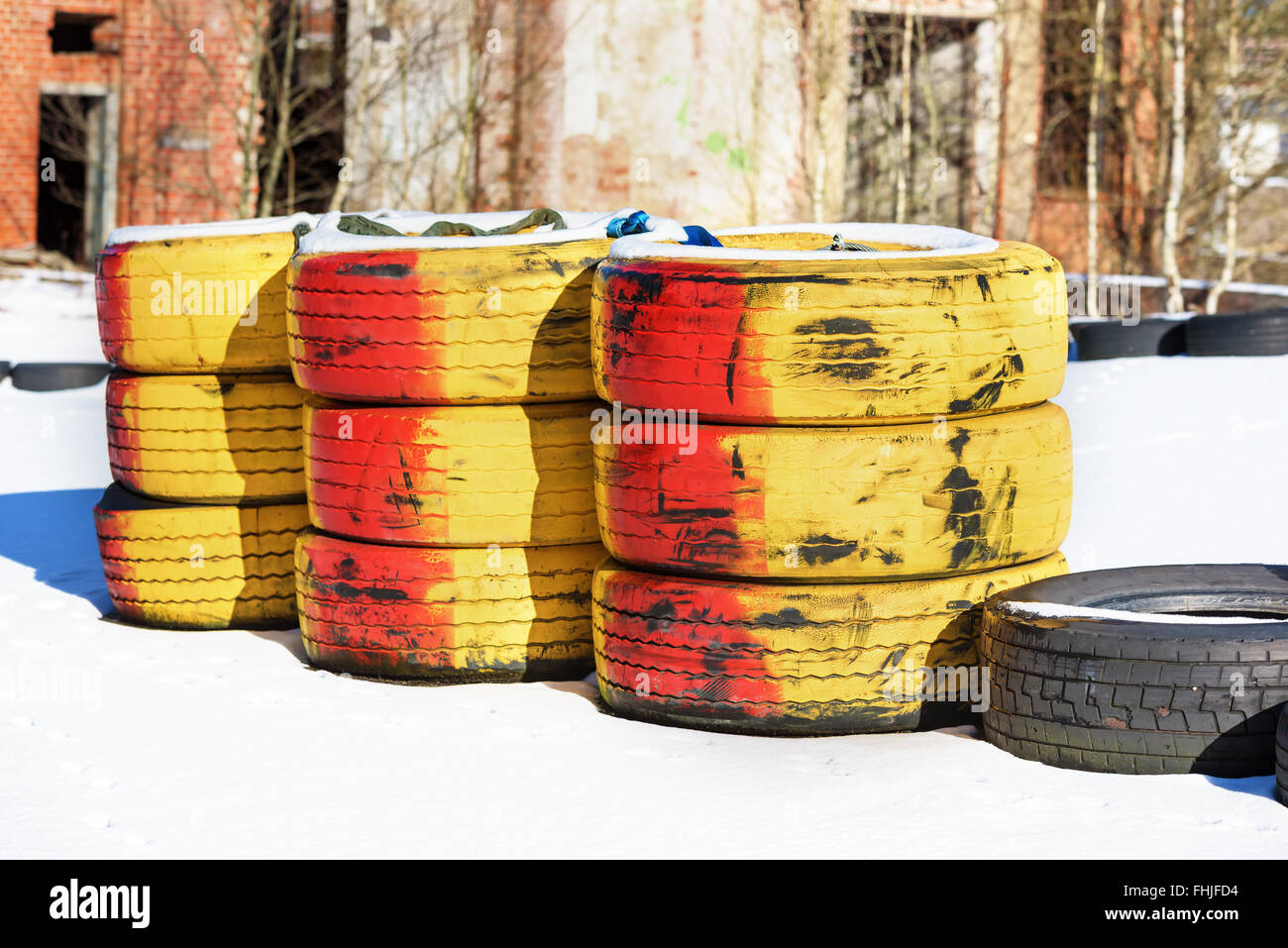 Three stacks of red and yellow painted car tires on the turn of a karting racing track. Some snow cover the track and industrial Stock Photo