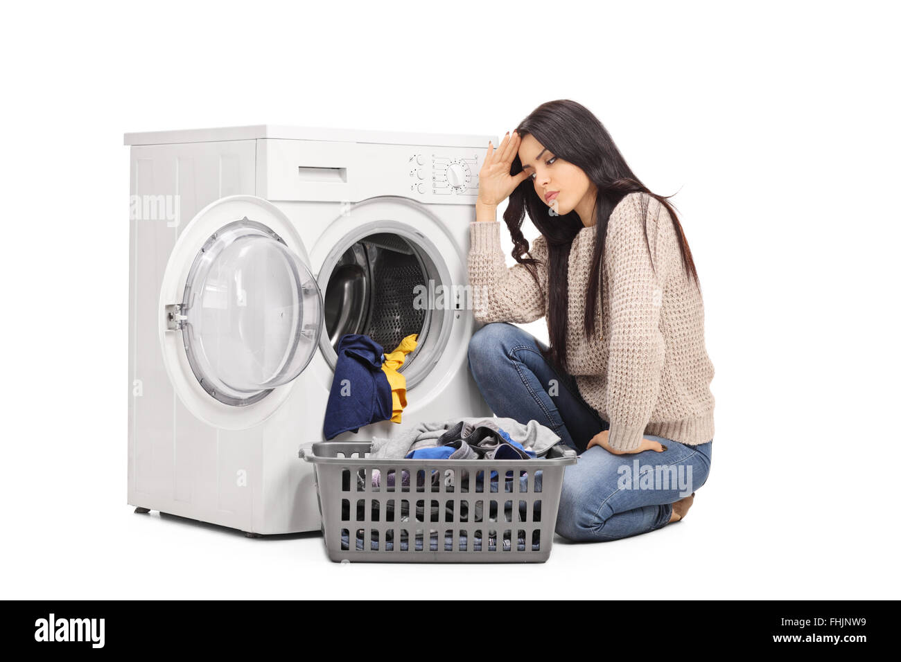Sad woman emptying a washing machine seated on the floor isolated on white background Stock Photo