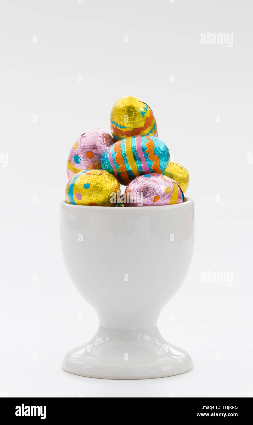 A white egg cup filled with small, chocolate Easter eggs on an isolated white background. Stock Photo