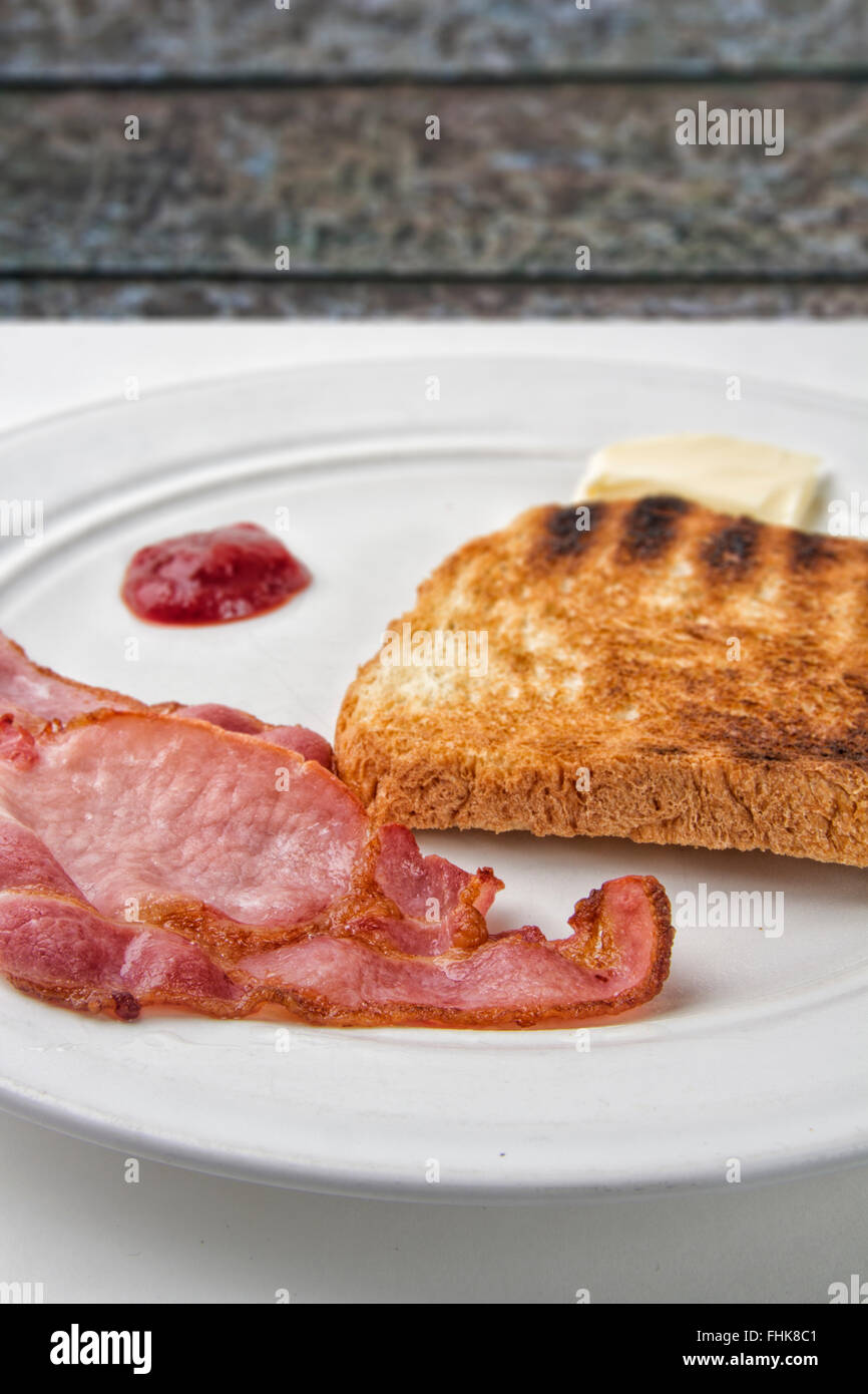 Two rashers of bacon and a slice of toast on a plate with butter and ...