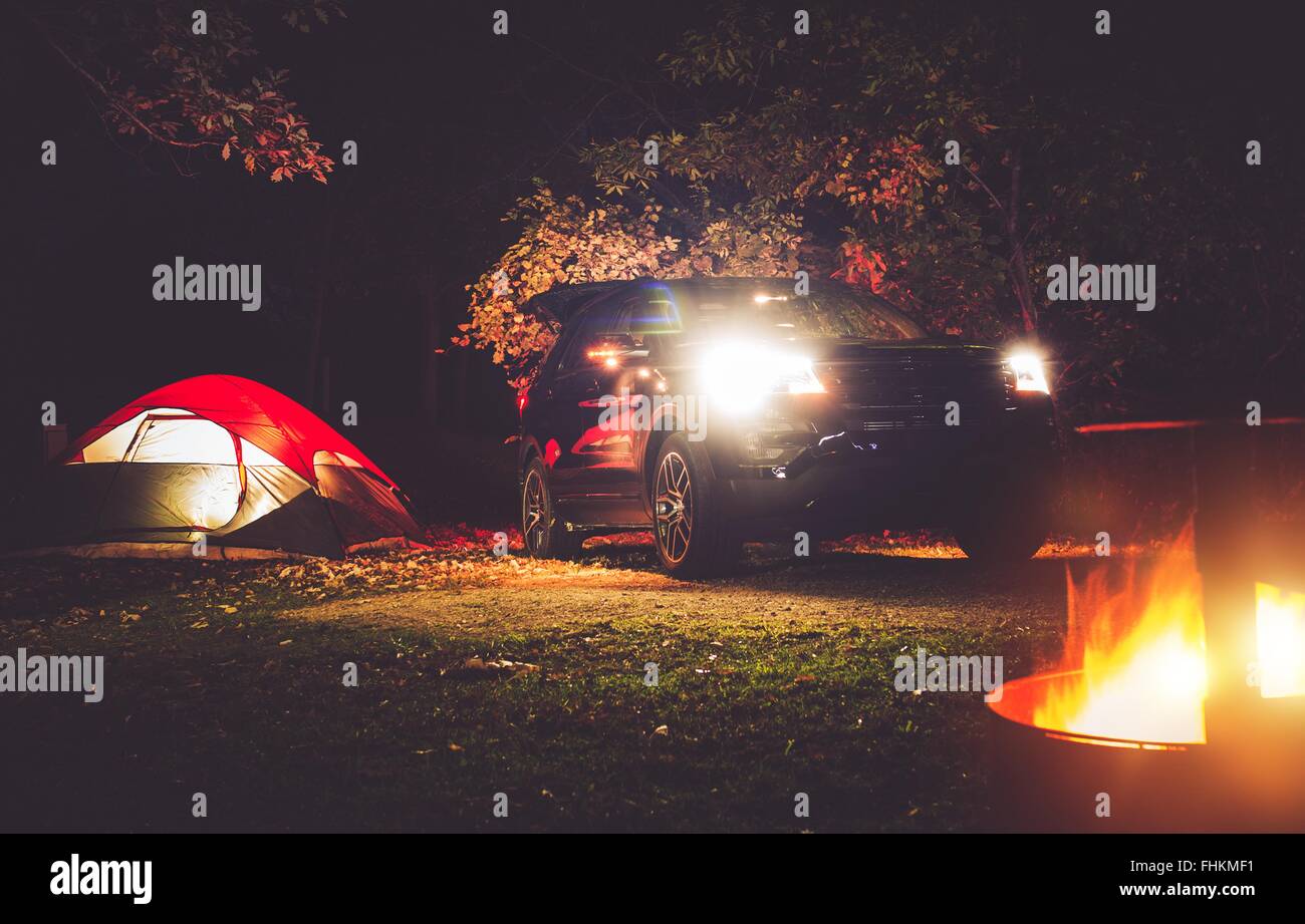 Camping Adventure. Tent Camping in the Deep Forest. Modern Offroad Car, Tent and Burning Wood in the Camping Fire Pit. Stock Photo
