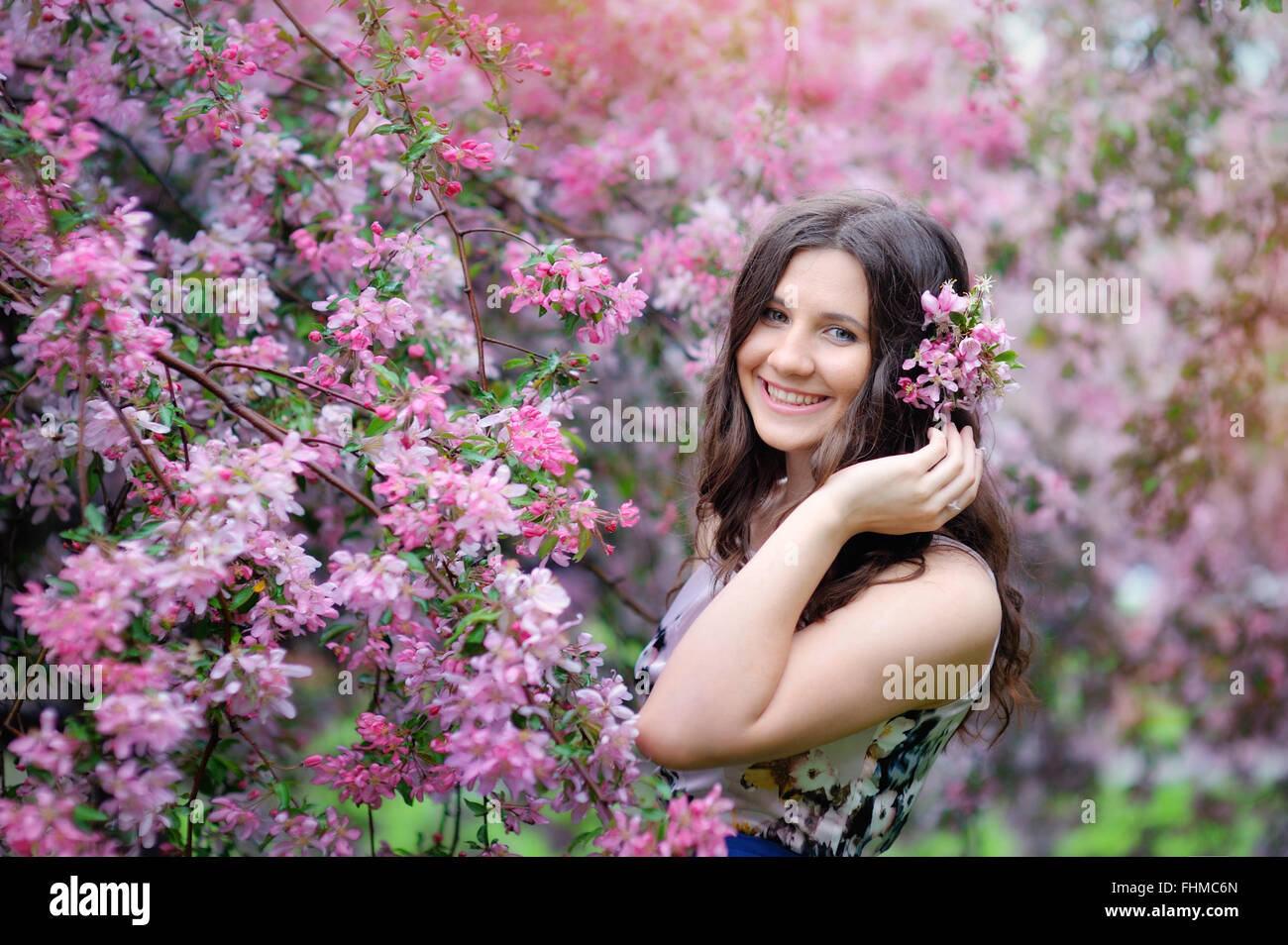 Beautiful girl in spring park with flowers lifestyle portrait, happy woman with blooming cherry tree. Skin care and beauty. Smiling teen girl in spring garden enjoying nature. Spring concept. Series. Stock Photo