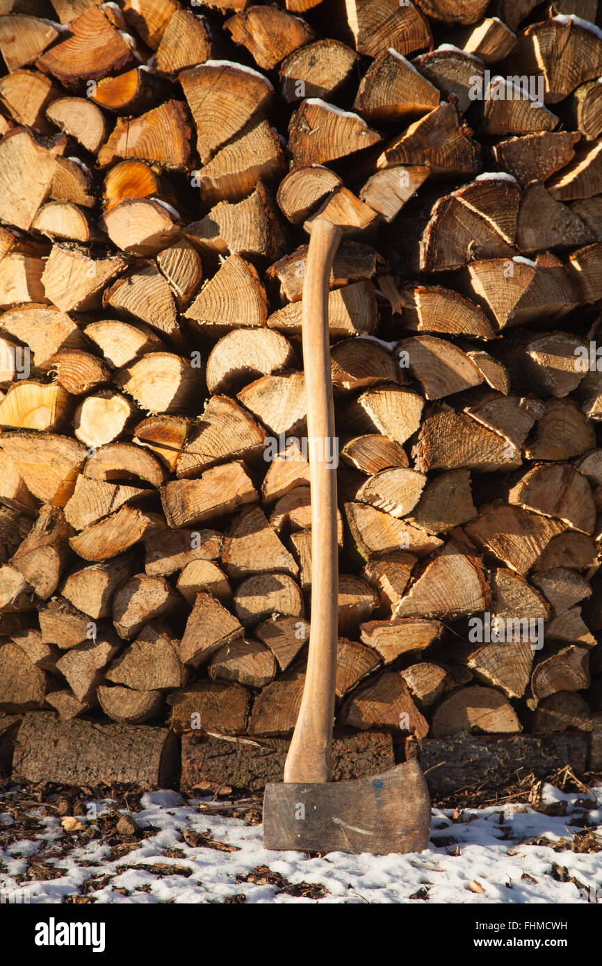 A wooden axe resting against a Holz Hausen wood pile in the snow. Stock Photo