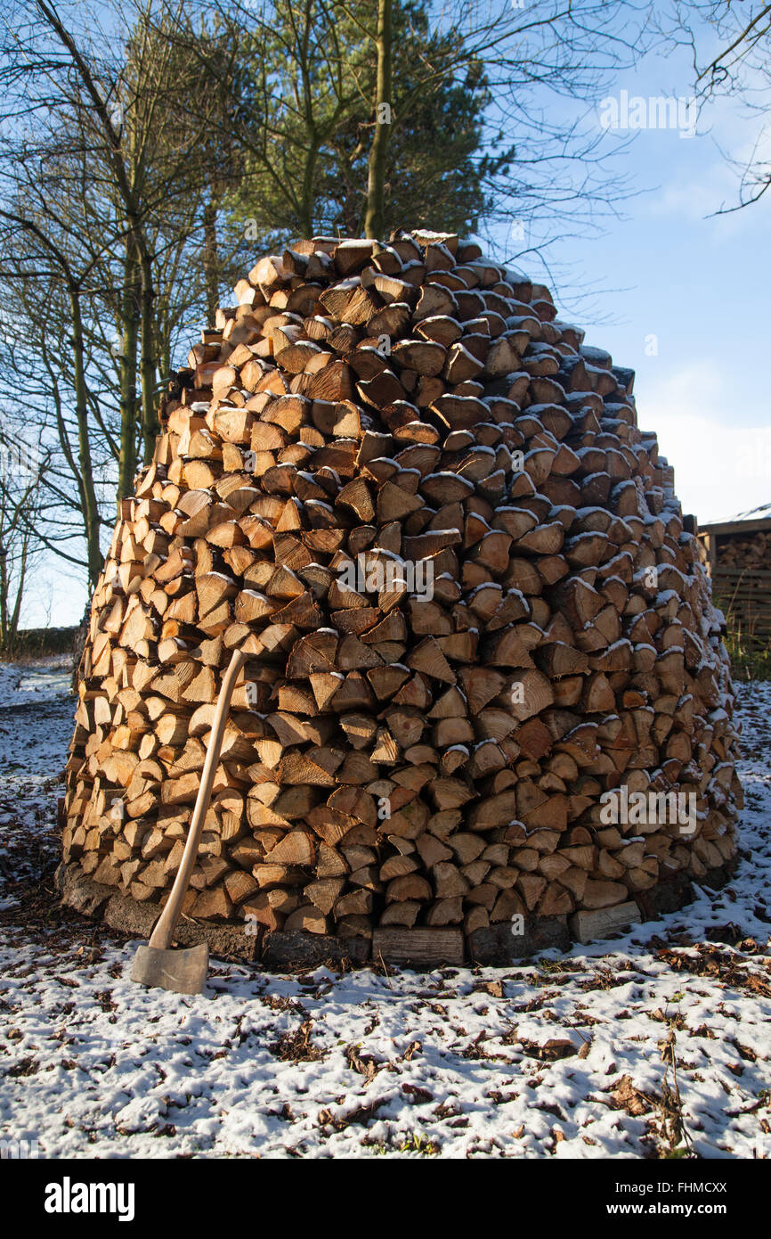 A wooden axe resting against a Holz Hausen wood pile in the snow. Stock Photo