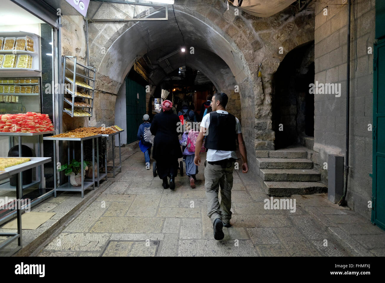 A religious Jewish family being escorted by security guard walk through Al Wad street which Israelis call Haggai street in the Muslim Quarter in the old city East Jerusalem Israel on 16 October 2015  The Housing Ministry has been funding security for settlers in East Jerusalem since the 1990s, through private security firms, who watch over ideological settlers who have implanted themselves in the heart of Palestinian neighborhoods in East Jerusalem. The number of Jews living in these areas is estimated at less than 3,000. Stock Photo