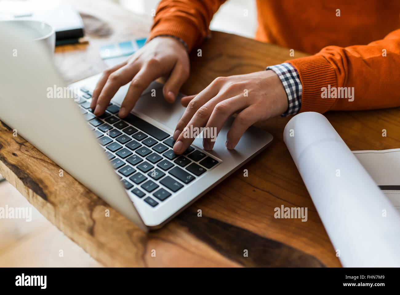 Close-up of man using laptop next to construction plan at desk Stock Photo