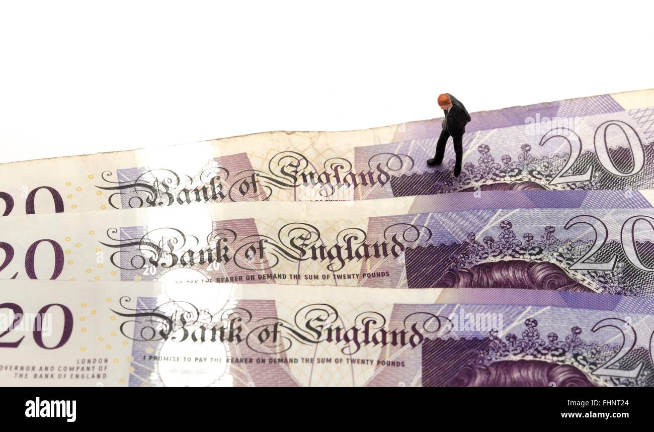 A miniature figurine business man in a suit looking down at the words Bank Of England on some twenty pound notes Stock Photo