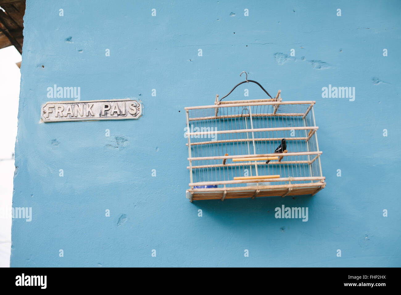 A caged bird hangs on the blue wall next to the street sign for Frank Pais in Trinidad, Cuba Stock Photo