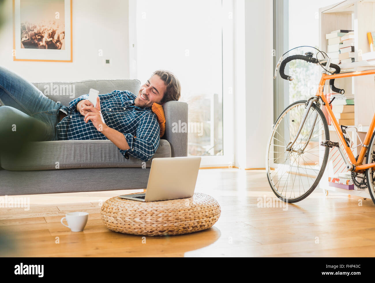 Young man lying on the couch at home looking at laptop Stock Photo