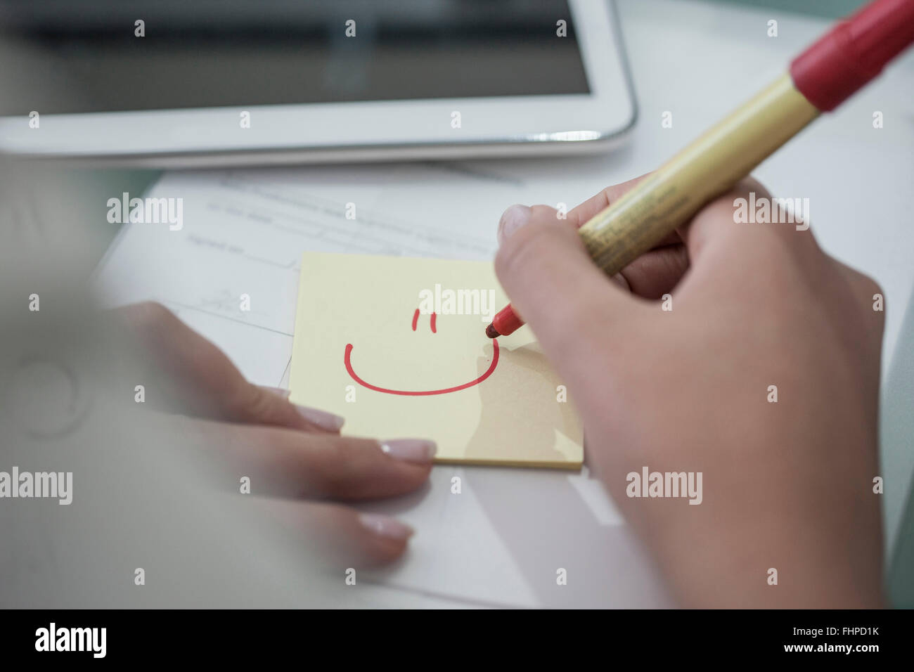 Close-up of woman at desk drawing a smiley face on sticky note Stock Photo