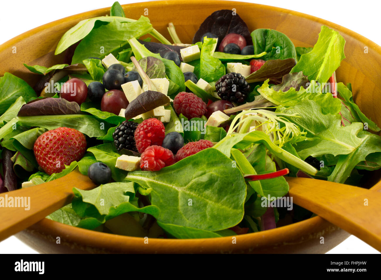 Organic mixed greens, berries and sprouted tofu salad served in wooden bowl, on white background