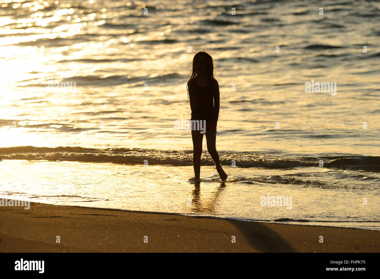 Beach girl silhouette is a striking silhouette of girl standing in the water at the beach. Stock Photo