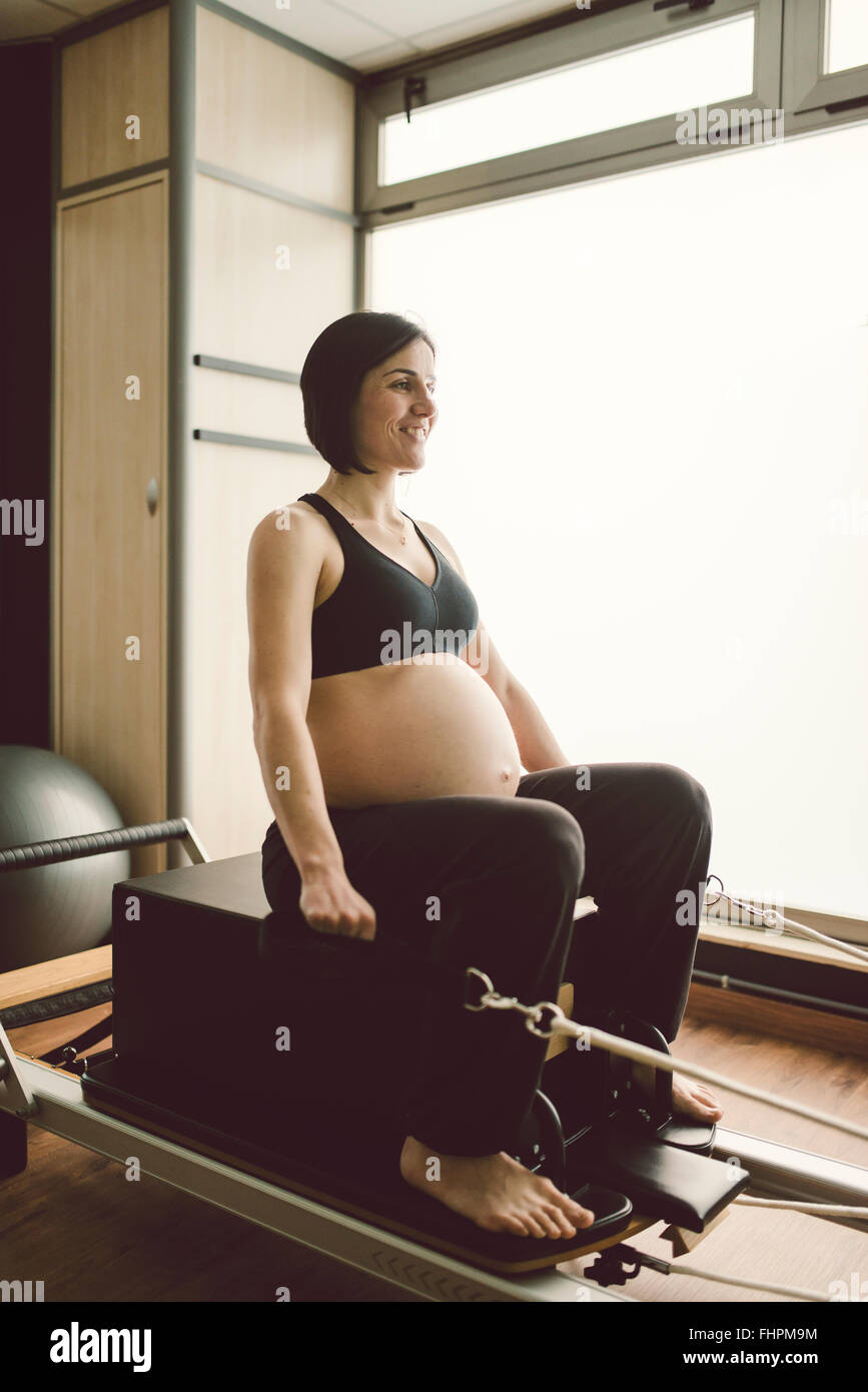 Pregnant woman doing Pilates exercises with a reformer pilates machine