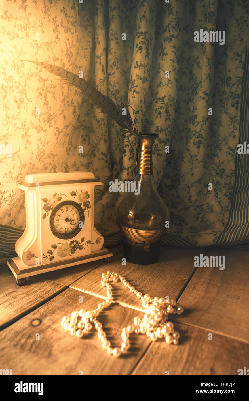 romantic still life with a vintage clock, glass bottle, feather and pearls Stock Photo