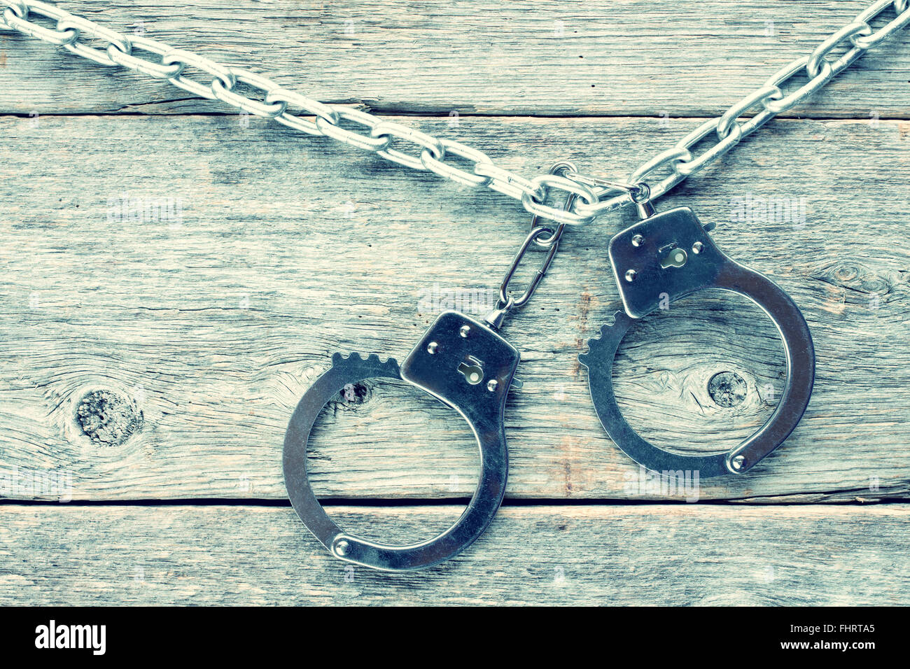 Handcuffs hanging on the chain against wooden wall.Filtered image. Stock Photo