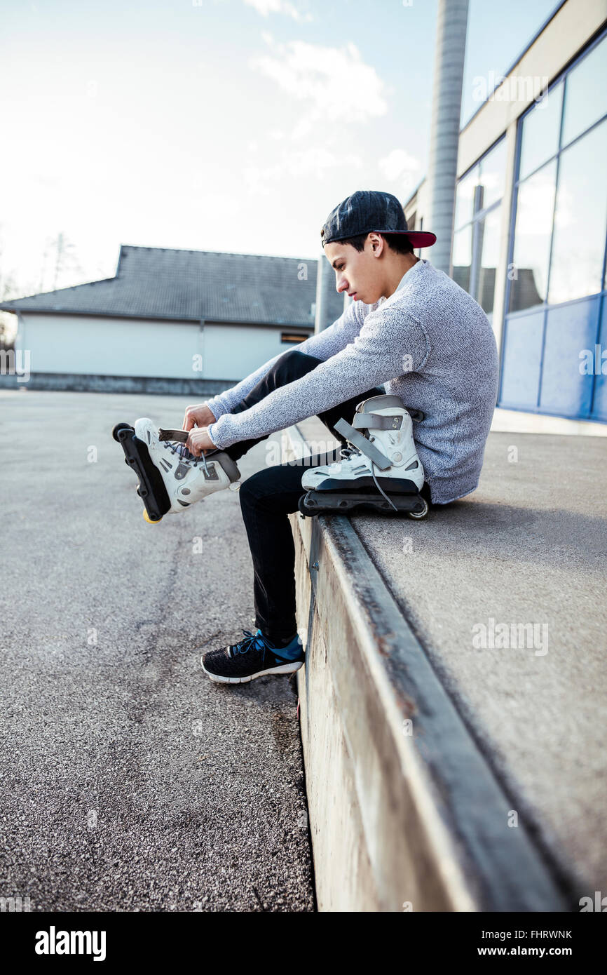 Young man sitting on ramp putting on inline skates Stock Photo
