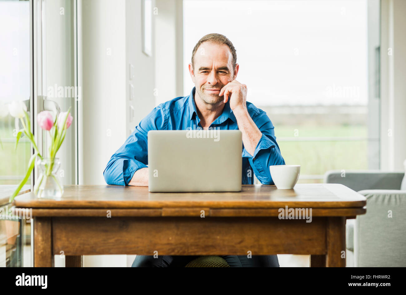 Businessman at home with laptop at wooden table Stock Photo
