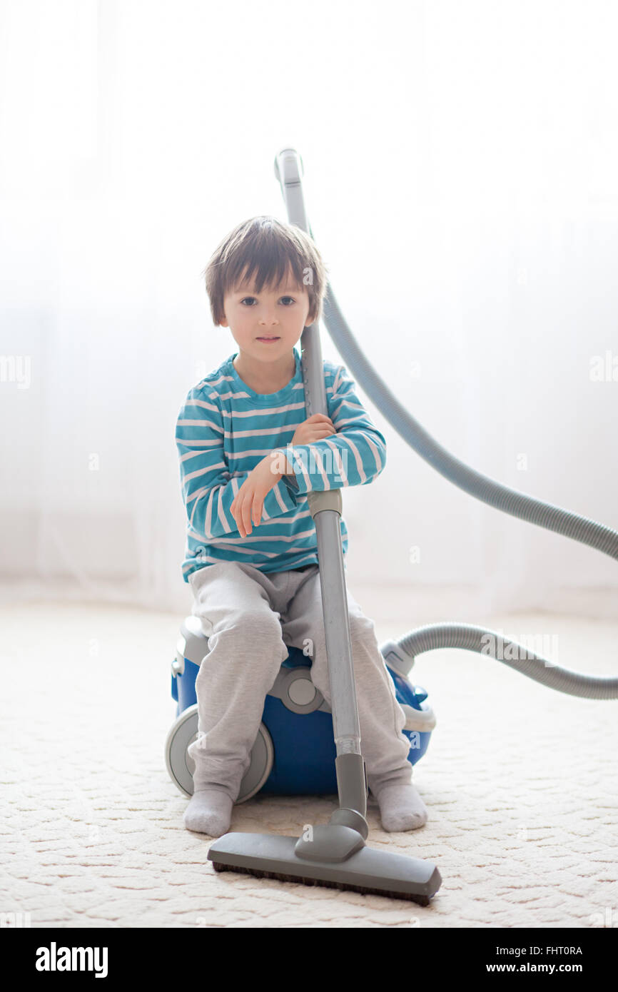 Sweet boy, playing with hoover at home, cleaning with vacuum cleaner