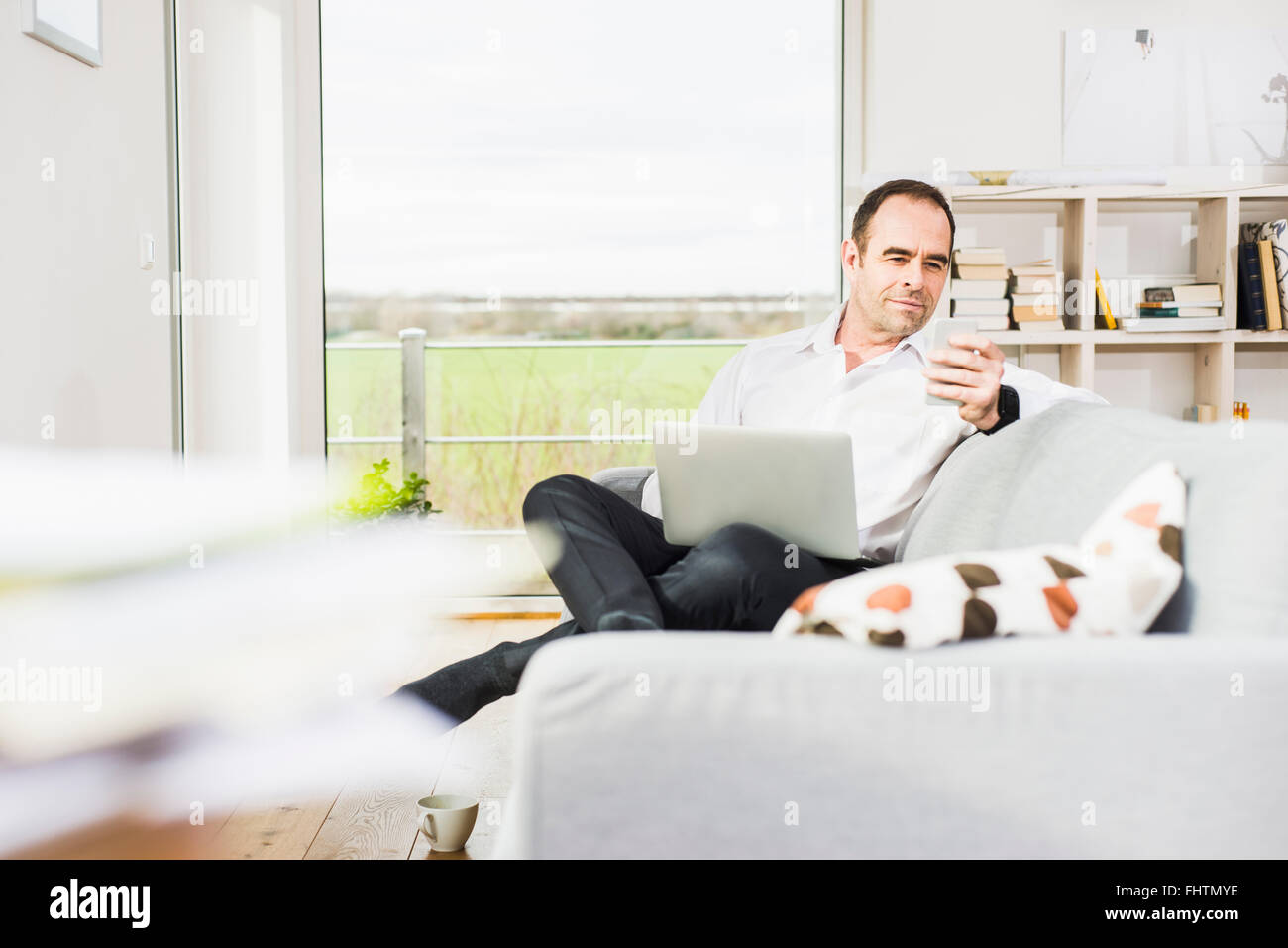 Businessman on couch using laptop and cell phone Stock Photo