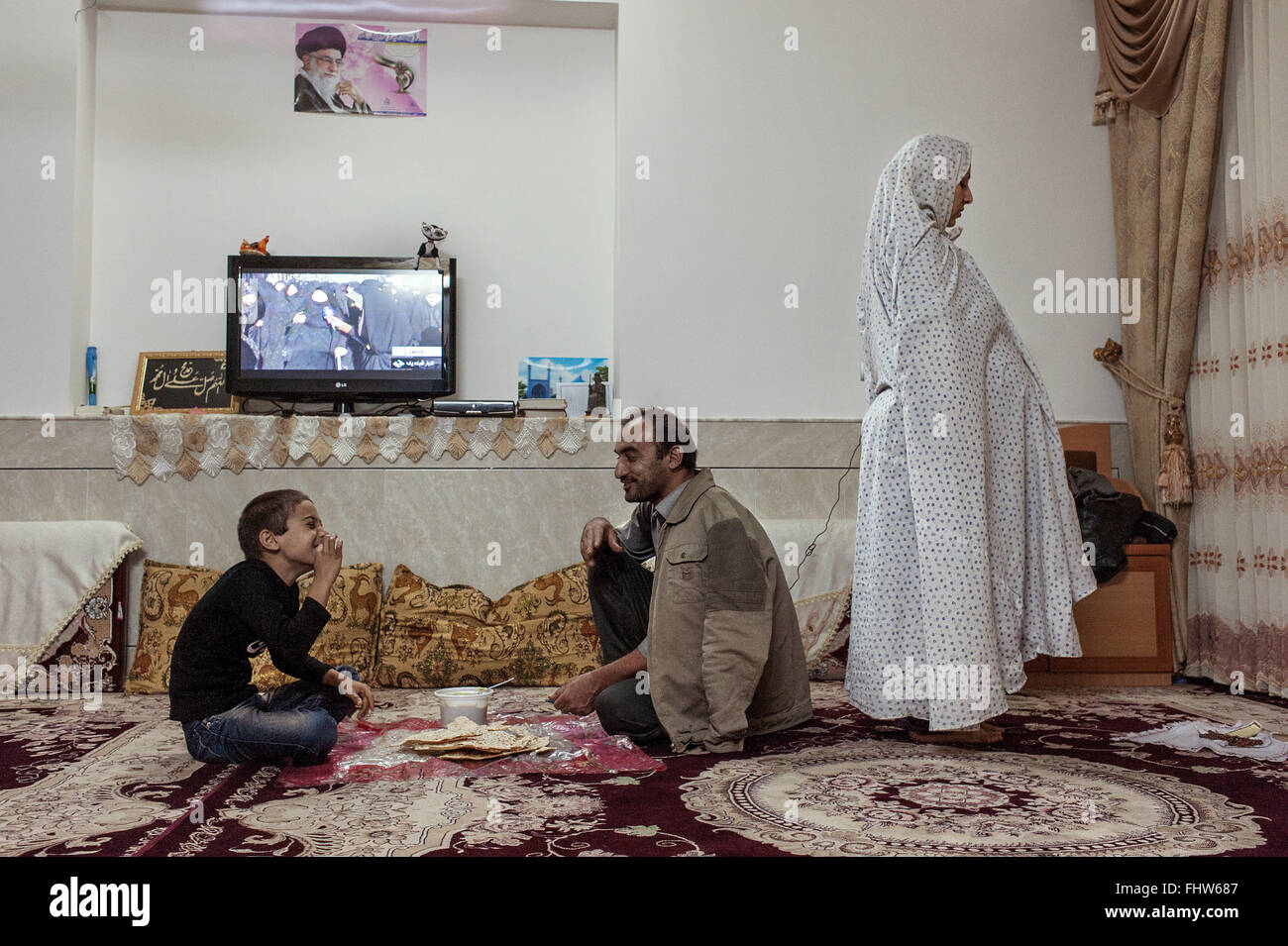 A Muslim Shia woman is reciting the fourth prayer of the evening, while the rest of the family is having dinner. In the background the television shows live from Kerbala the ceremony of Ashura. (Photo by Claudia Borgia / Pacific Press) Stock Photo