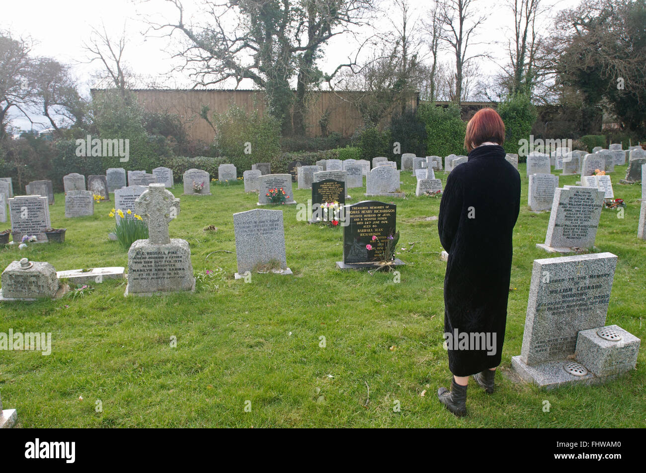 A woman looking at headstones in a graveyard in Cornwall, UK Stock Photo