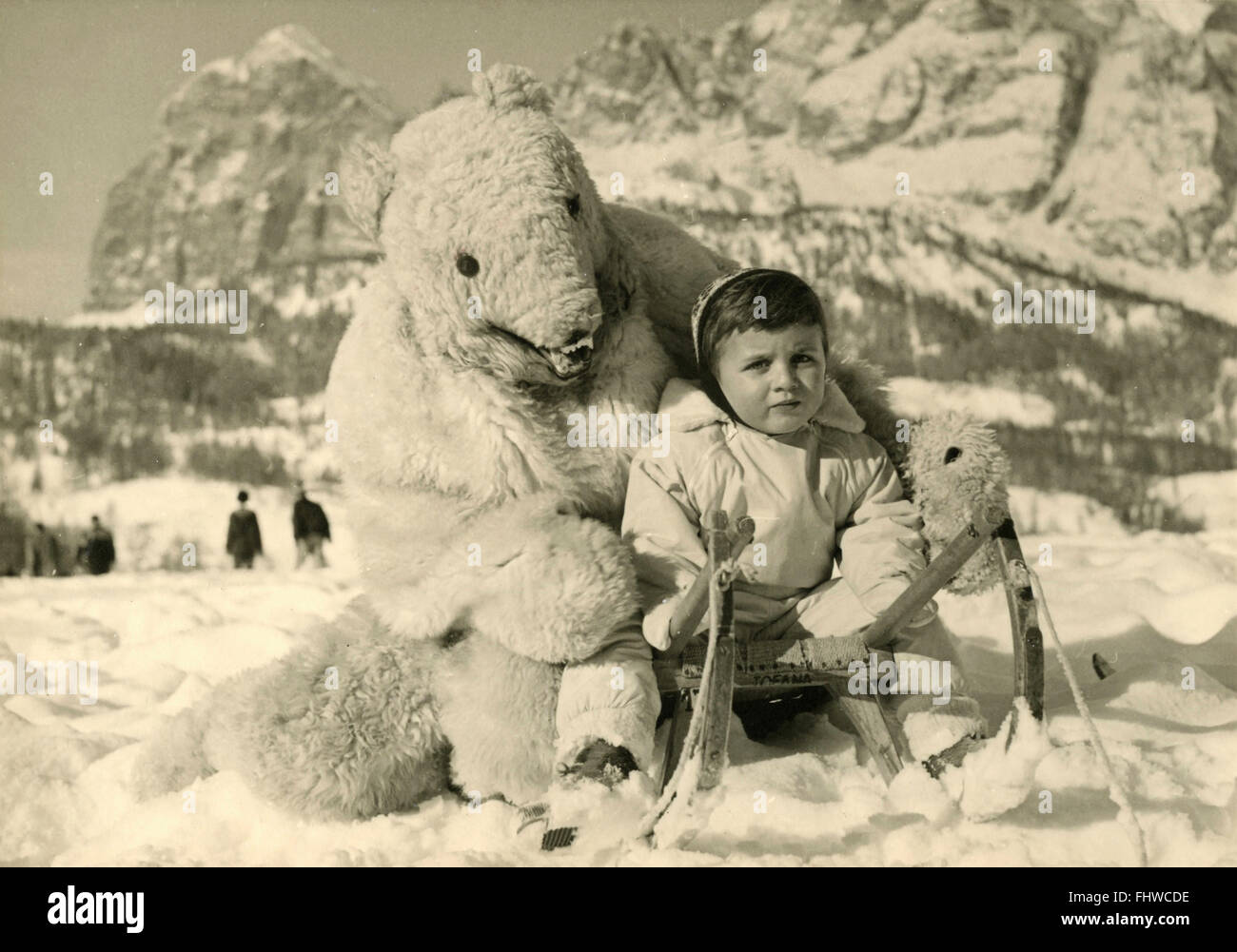A child with a sled on the snow and a man disguised as a bear, Cortina, Italy Stock Photo