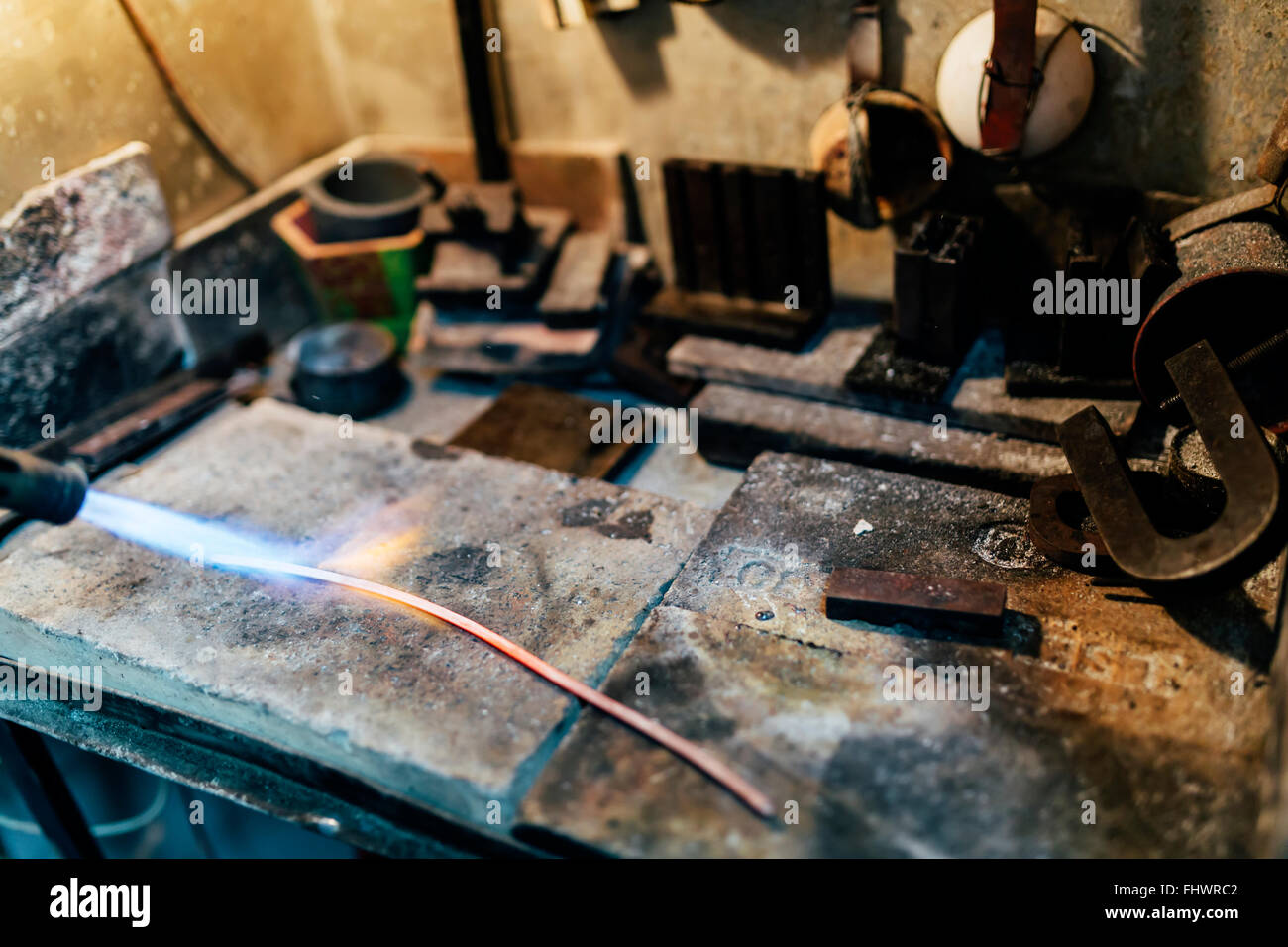 Craft jewelry with a torch flame against a dark background. Jeweler handles  metal rail by heating it.Beautiful bright close up photo. Stock Photo