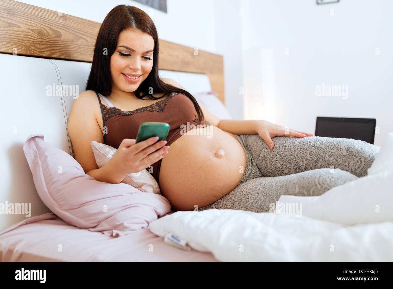Pregnant woman using phone while lying on bed and resting Stock Photo