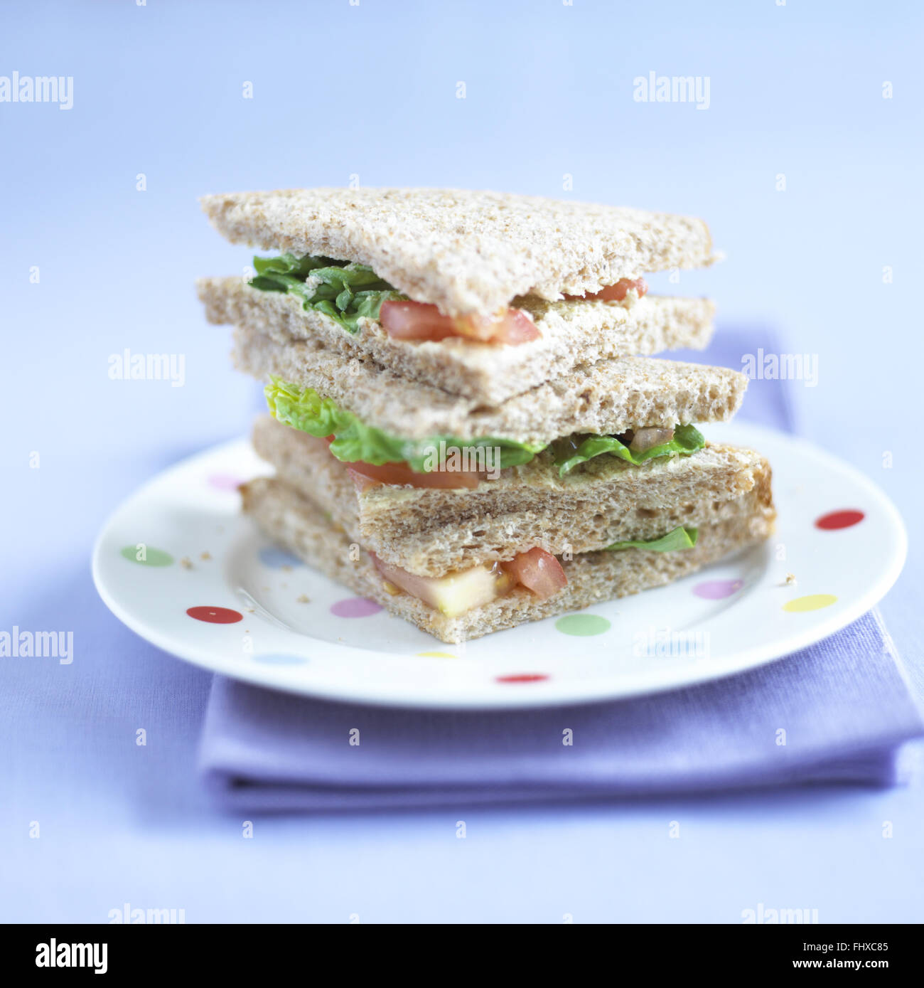 Three triangular sandwiches piled up on dotted plate, purple napkin underneath. Stock Photo