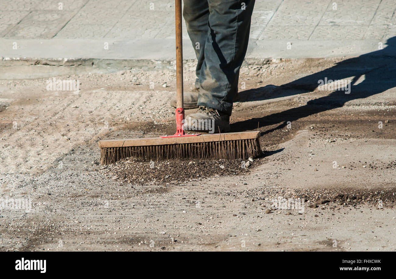 worker with large scrub brush collect residues of asphalt milling Stock Photo