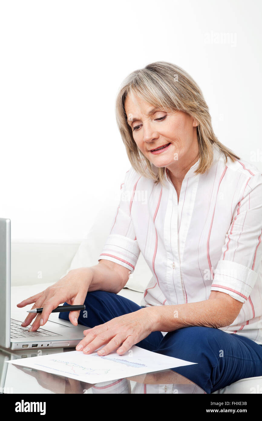 Happy senior woman working on laptop with stock prices Stock Photo