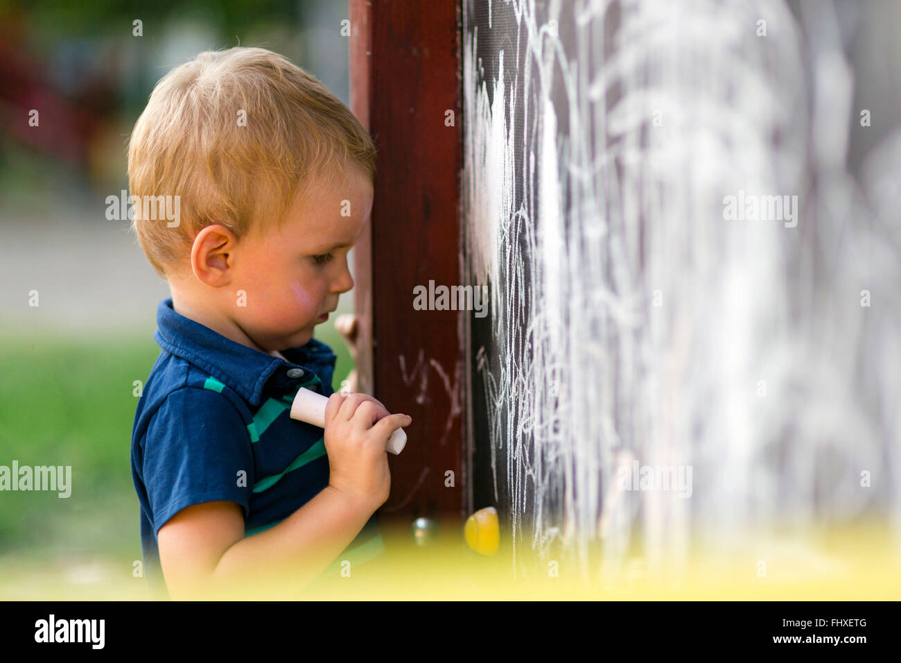 Creative cute toddler drawing with chalk outdoors on a drawing board Stock Photo