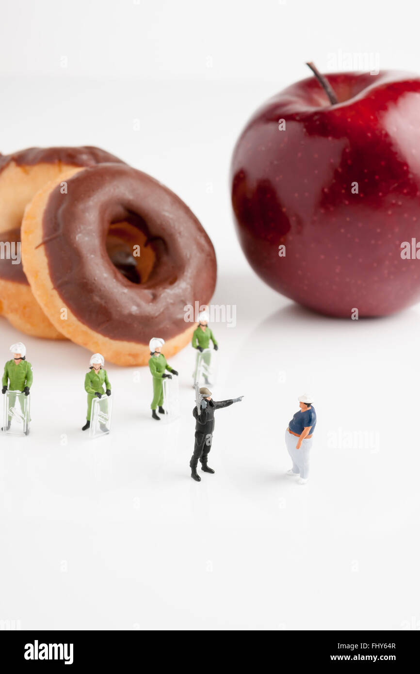 Tiny riot police telling a fat man to eat an apple instead of donuts an obesity or nanny state concept Stock Photo