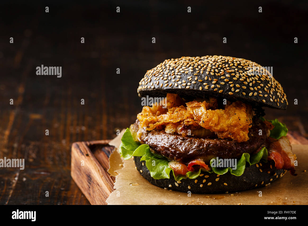 Black burger with sesame seed bun meat bacon and onion rings fries on dark wooden background Stock Photo
