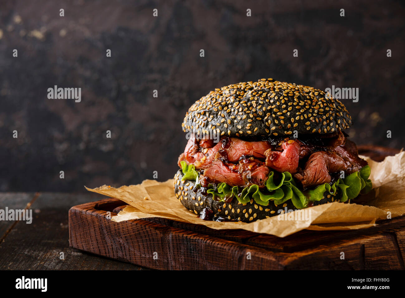 Roast beef Burger Takeaway snack on sesame bun with sliced Pastrami on black background Stock Photo